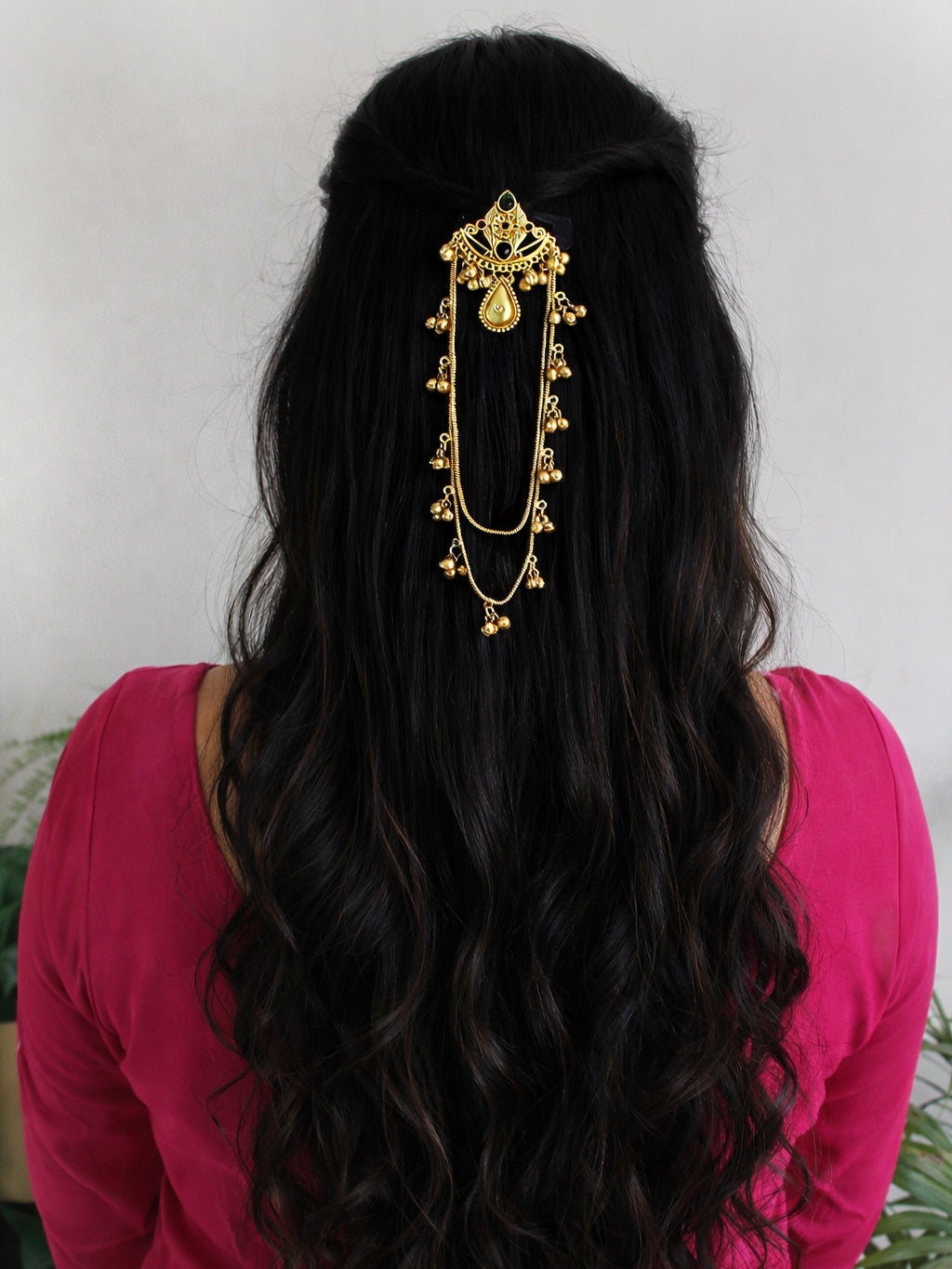 Person with long black hair wearing a gold hair accessory against a white background